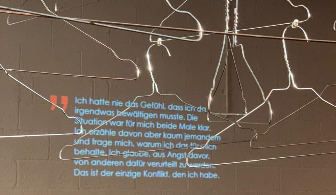 Hängende Kleiderbügel, im Hintergrund Text auf die Wand projeziert.