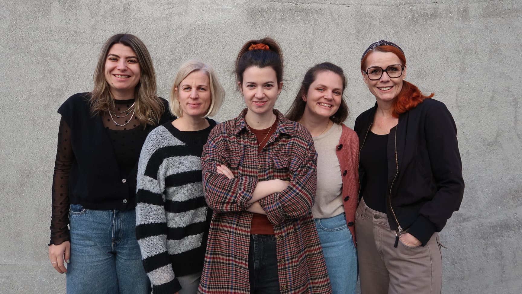 Fünf Frauen stehen vor einer Wand und lächeln in die Kamera.