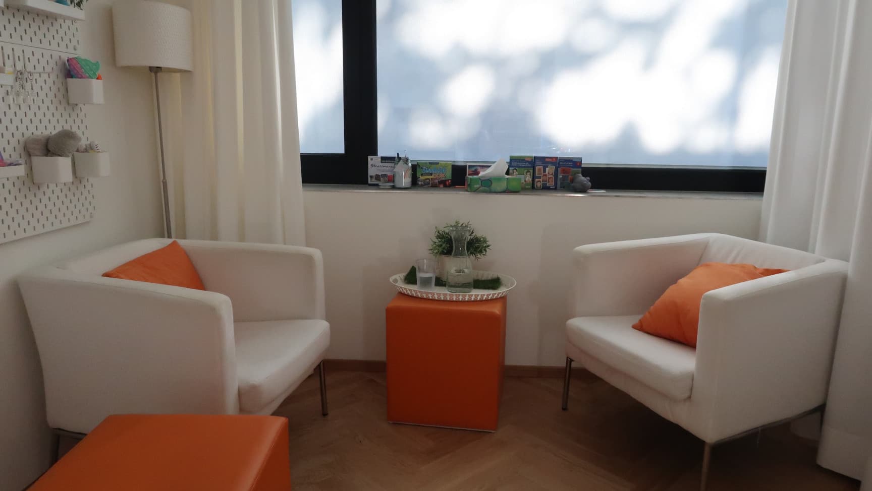 Zwei Sessel mit Kissen vor einem Fenster. In der Ecke eine Lampe, vor dem Fenster Vorhänge.