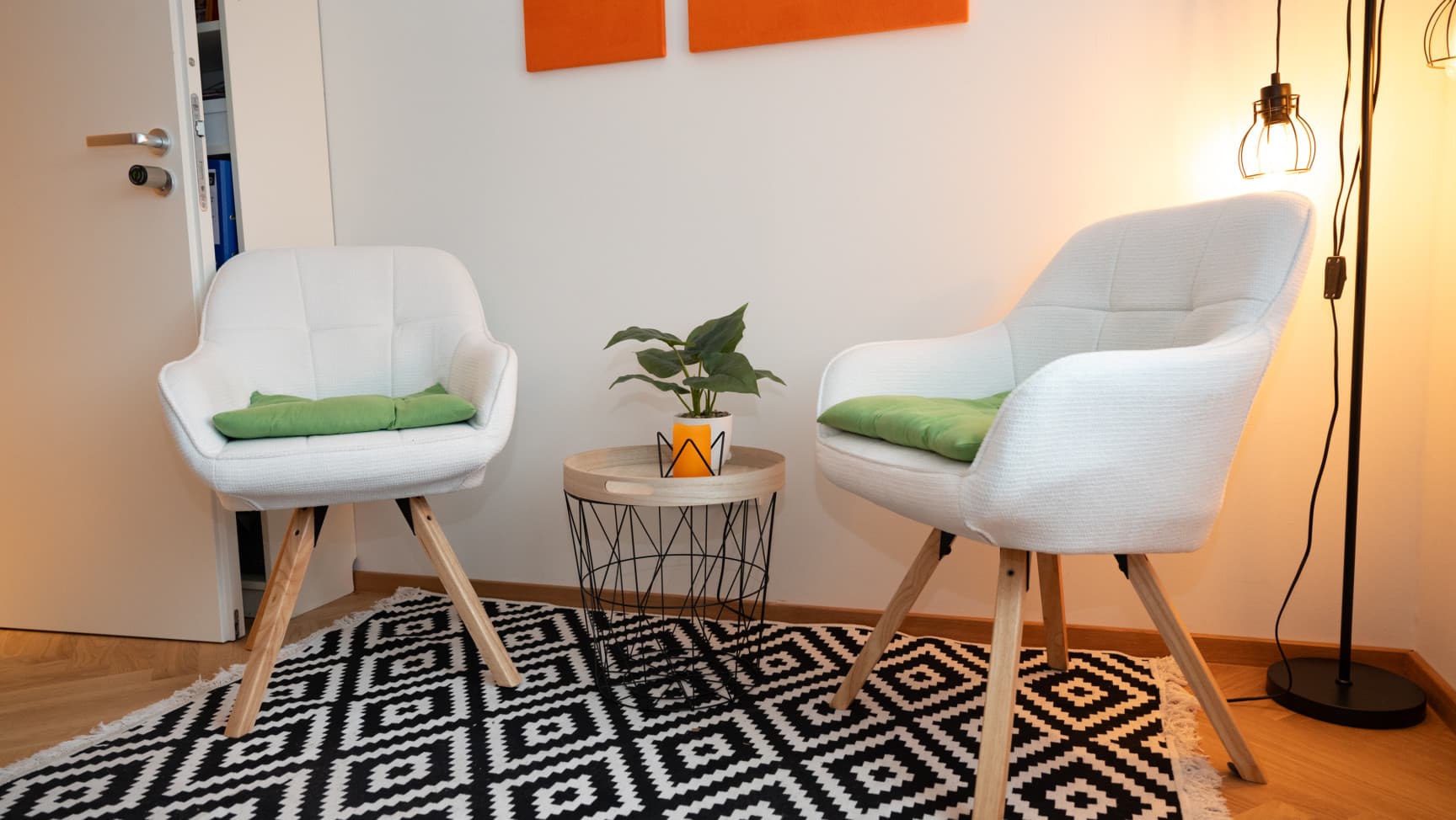 Zwei Sessel, ein kleines Tischchen mit Pflanze stehen auf einem Teppich. In der Ecke ist eine Lampe.