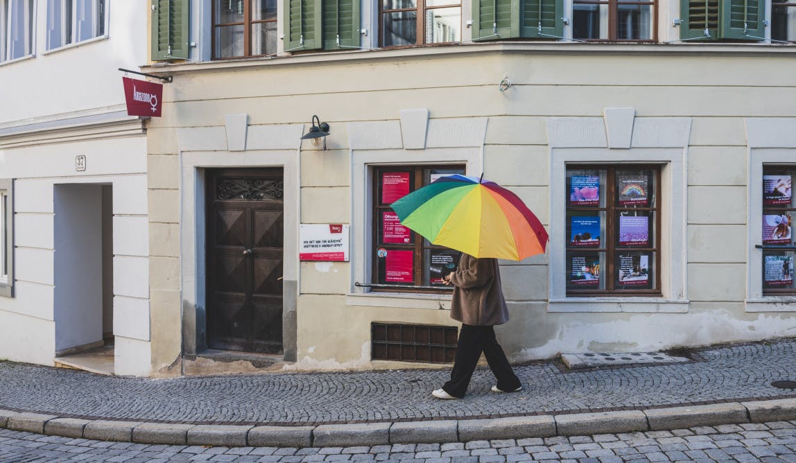 eine Person mit regenbogenfarbigem geht an einer Hausfassade vorbei