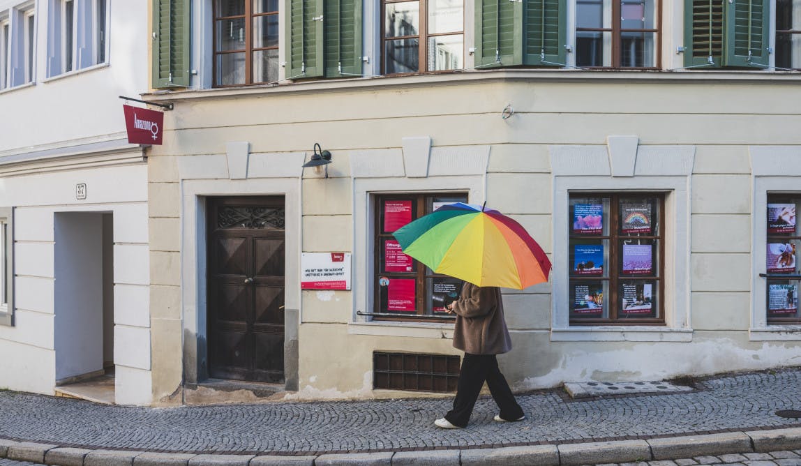 eine Person mit regenbogenfarbigem geht an einer Hausfassade vorbei