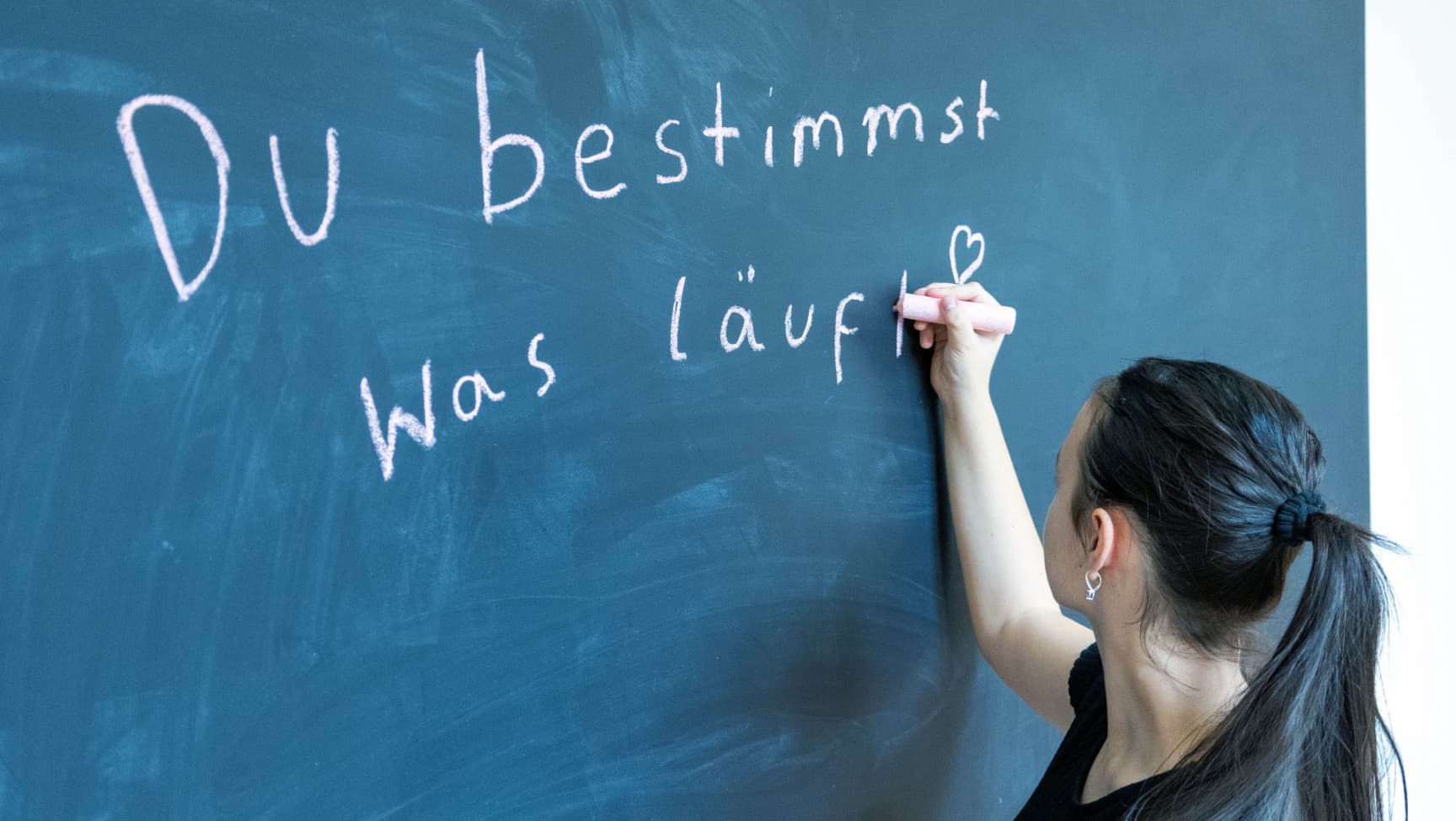 Eine jugendliche Person schreibt "Du bestimmst was läuft" auf eine Tafel.