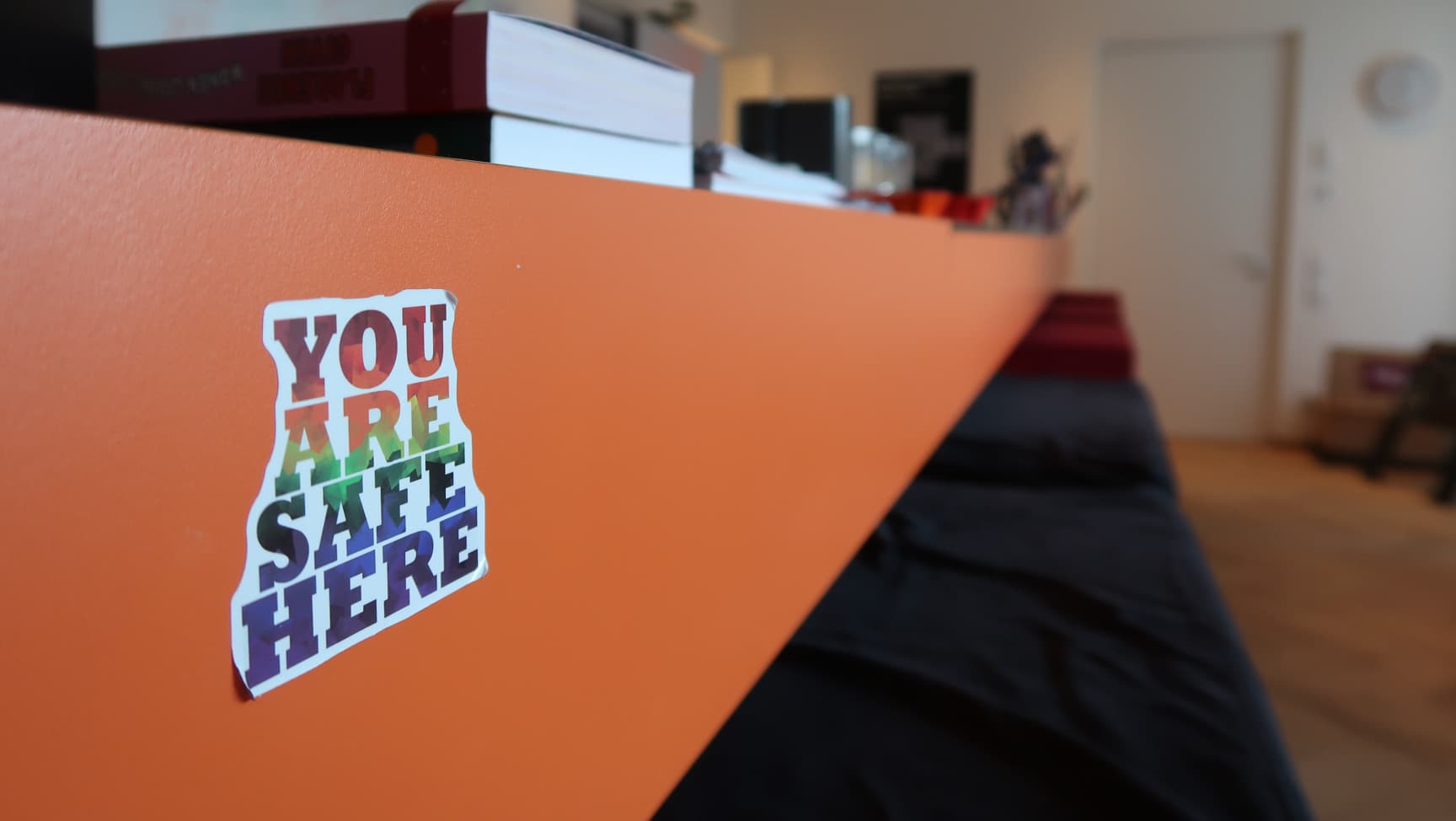 Ein unscharfer Raum, im Vordergrund klebt ein Sticker mit dem Schriftzug: You are safe here.