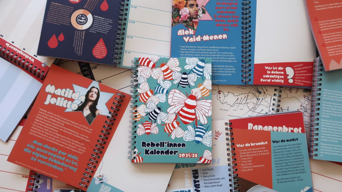 Ein Rebell*innen Kalender liegt inmitten vieler aufgeschlagener Kalenderseiten.