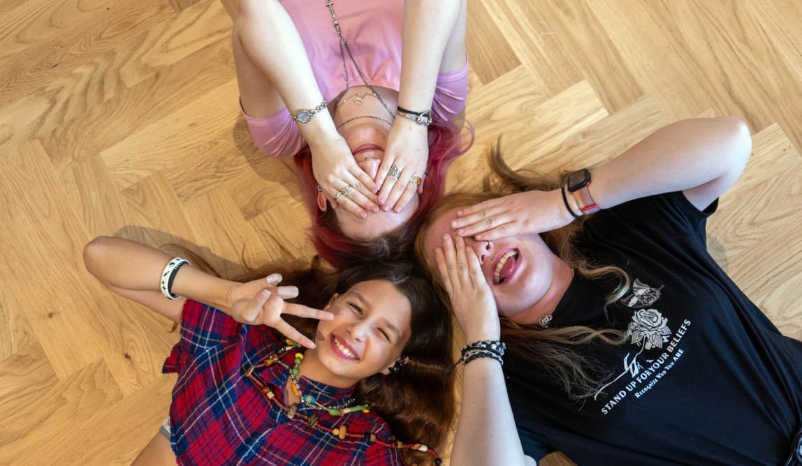 Drei Jugendliche liegen auf dem Boden. Zwei halten sich die Hände vor die Augen. Sie haben Spaß.