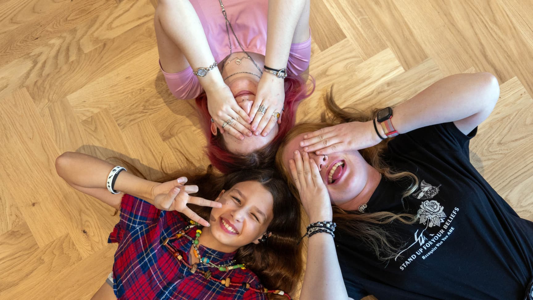 Drei Jugendliche liegen auf dem Boden. Zwei halten sich die Hände vor die Augen. Sie haben Spaß.