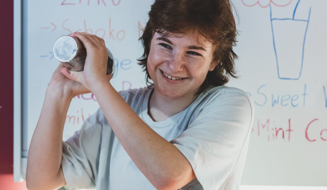 Eine jugendliche Person shakt einen Cocktail und lacht dabei.