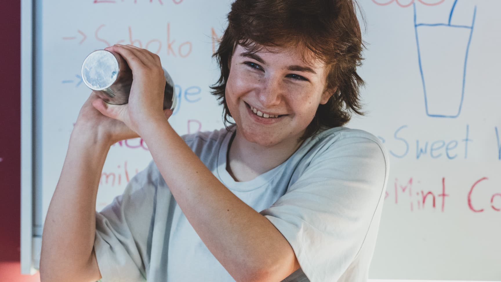 Eine jugendliche Person shakt einen Cocktail und lacht dabei.