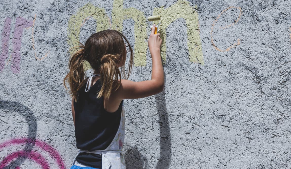 Eine jugendliche Person ist von hinten zu sehen, wie sie auf eine Wand mit einer Farbrolle gelbe Farbe aufträgt.