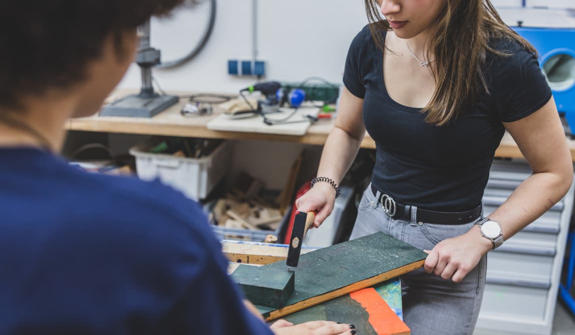 Junge Frau schlägt mit Hammer Nagel in Werkstück.