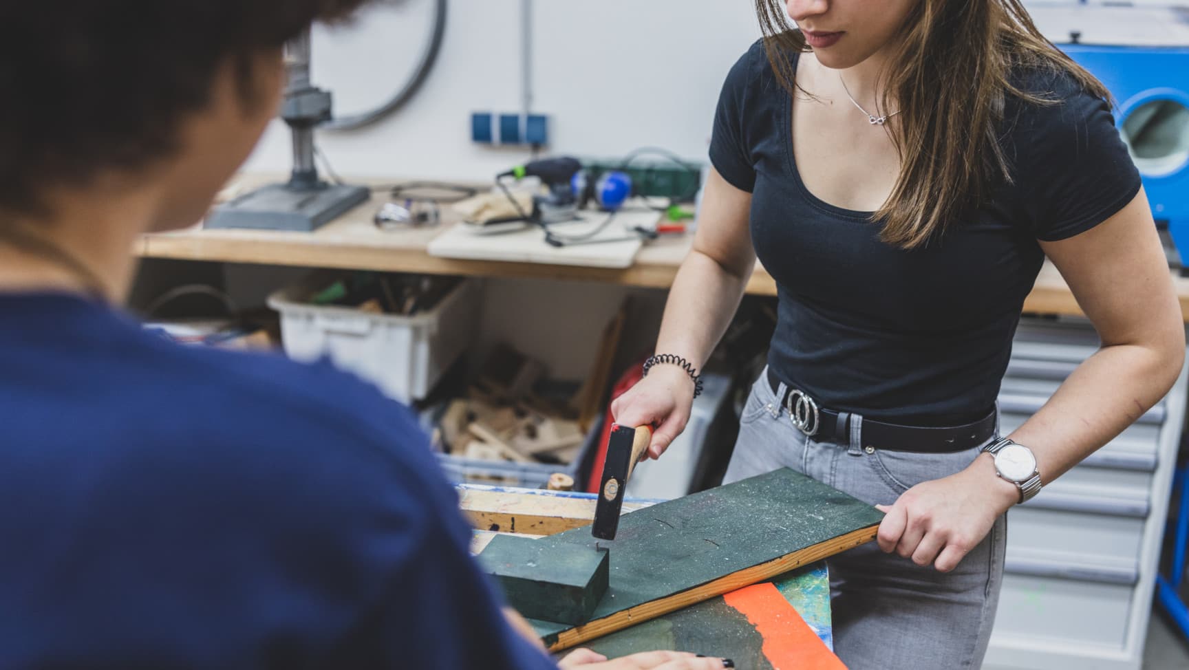 Junge Frau schlägt mit Hammer Nagel in Werkstück.