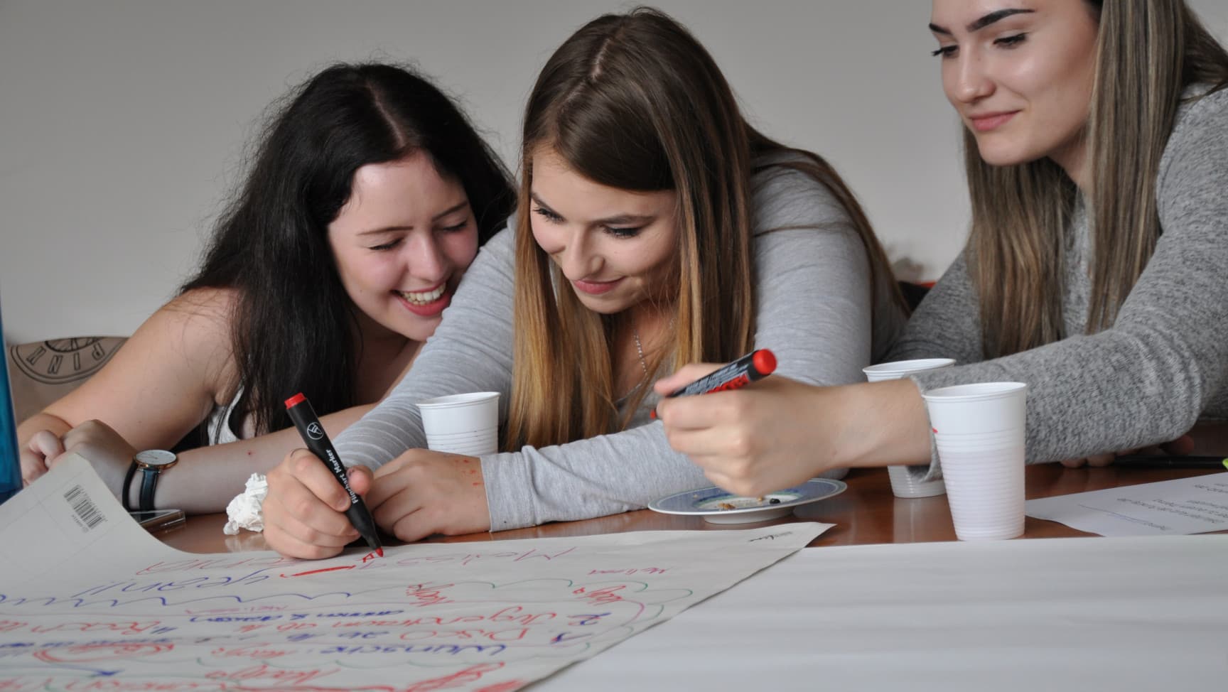 Drei junge Frauen* schreiben auf ein Flipchart