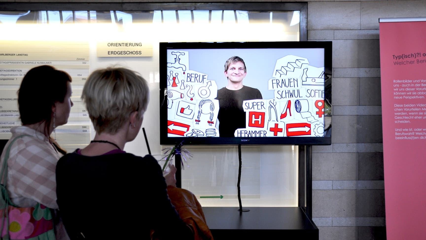 Zwei Personen schauen sich ein Video auf einem Monitor an