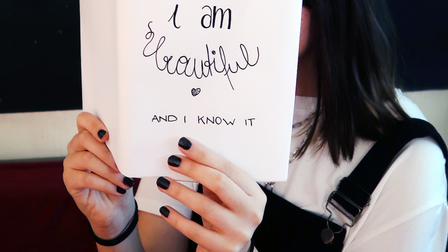 Mädchen hält aufgeschlagenes Buch mit dem Titel „I am beautiful“ vor ihr Gesicht.
