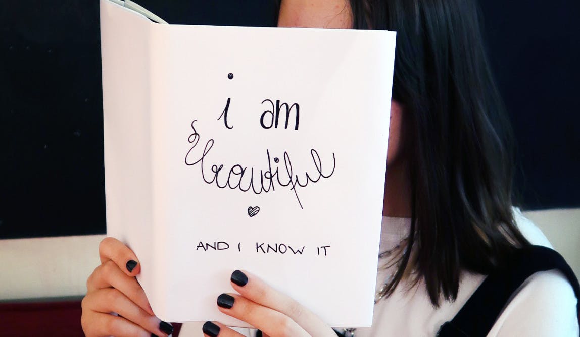 Mädchen hält aufgeschlagenes Buch mit dem Titel „I am beautiful“ vor ihr Gesicht.