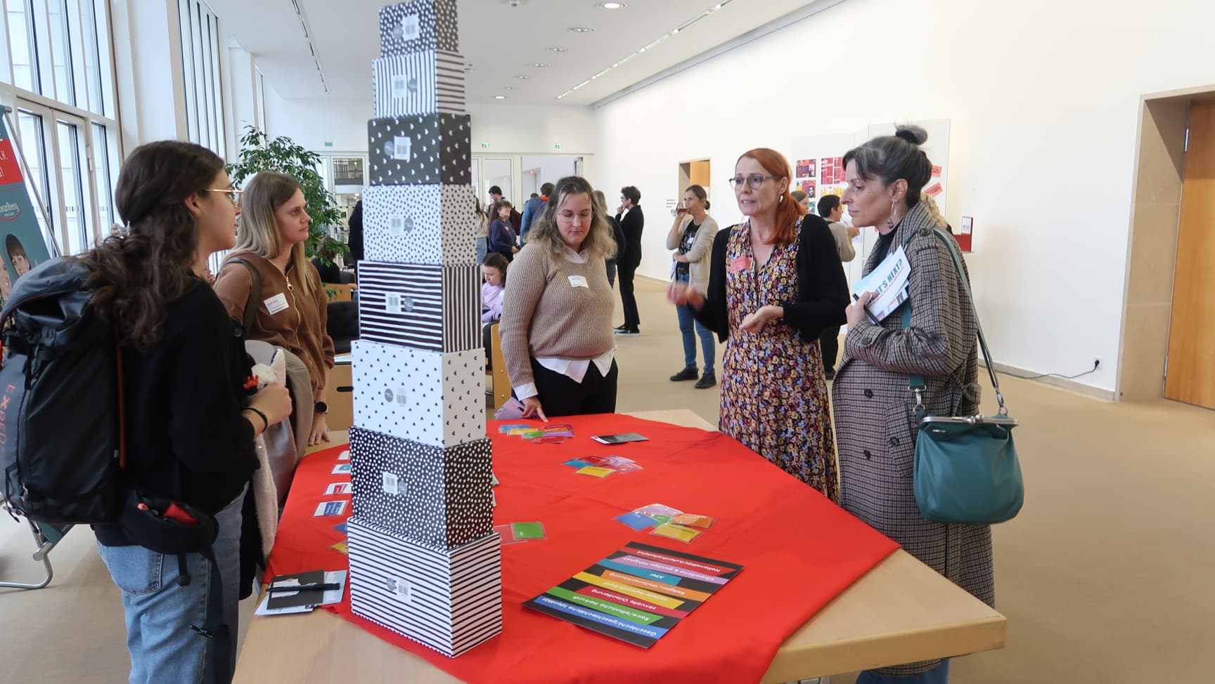 Frauen* stehen um einen Tisch, der belegt ist mit Karten und Schachteln