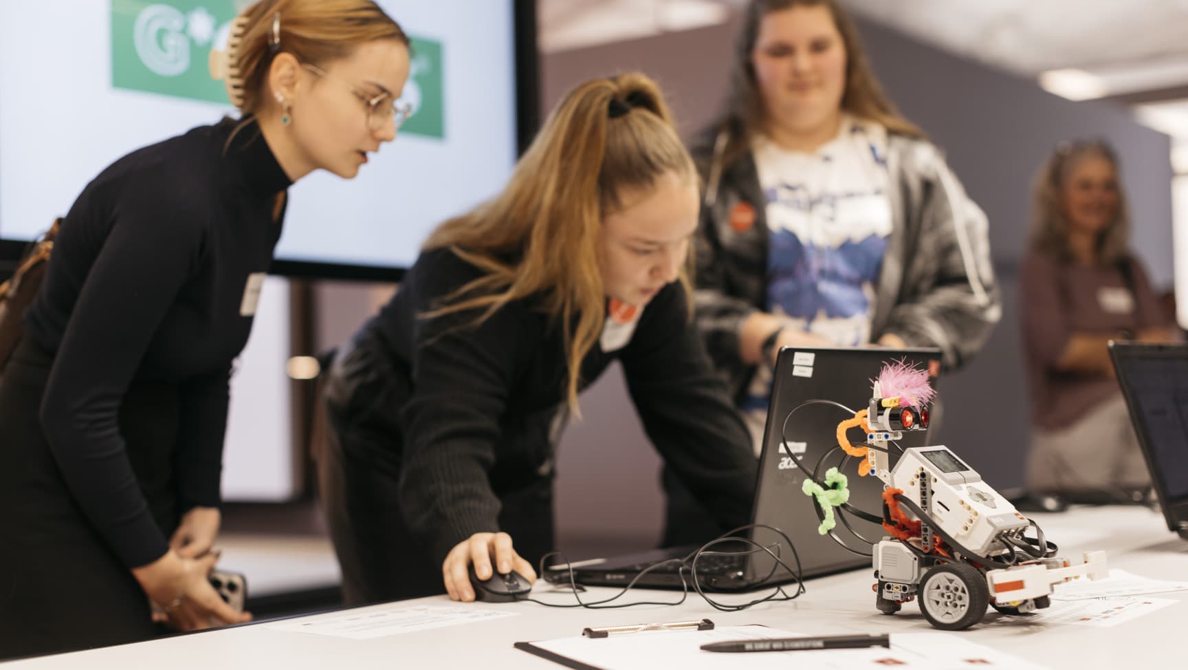 Lehrmädchen am Computer, vor ihnen ein Lego Roboter