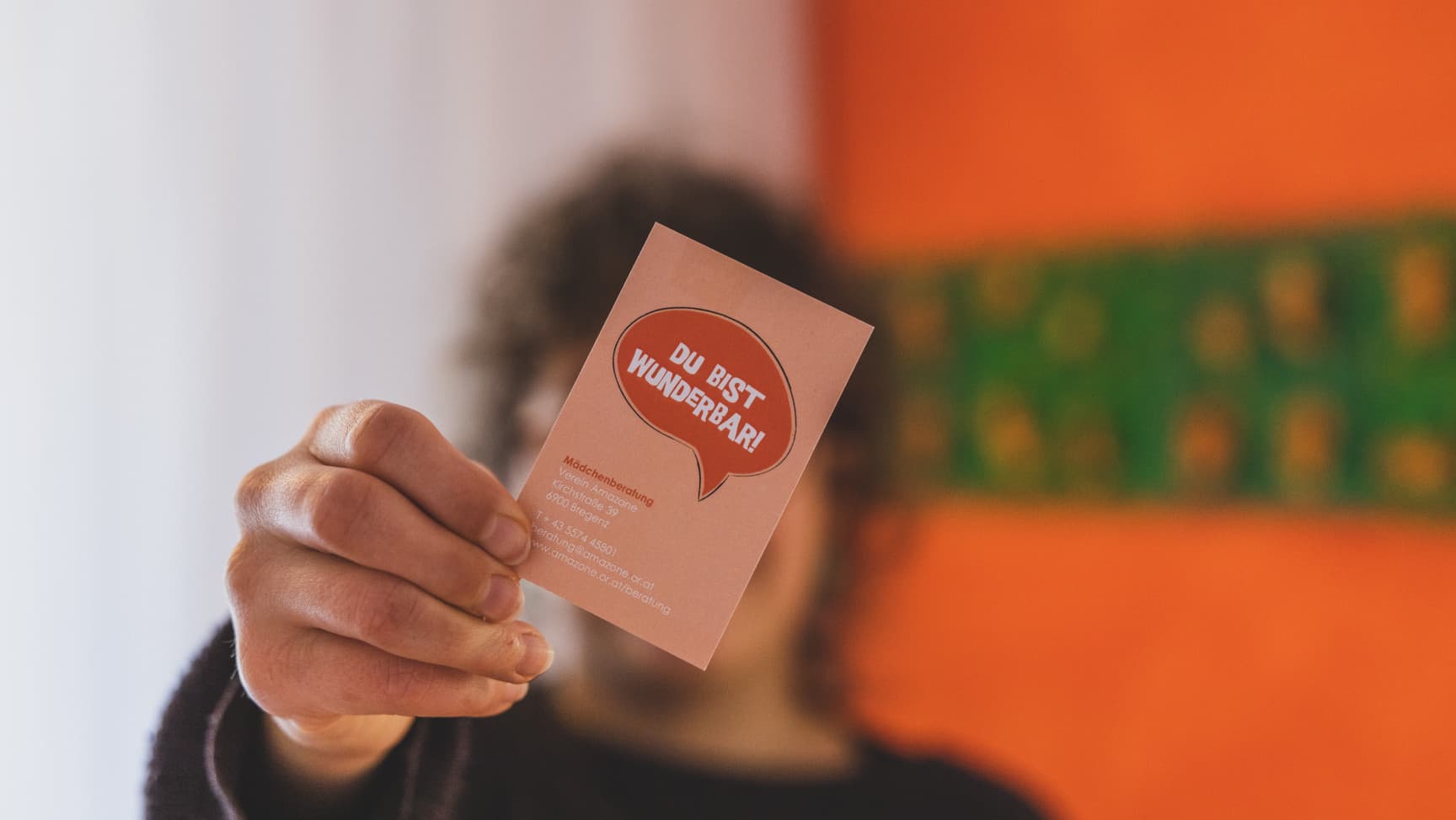 Eine Person hält eine orange Karte mit der Aufschrift „Du bist wunderbar“ in die Kamera.