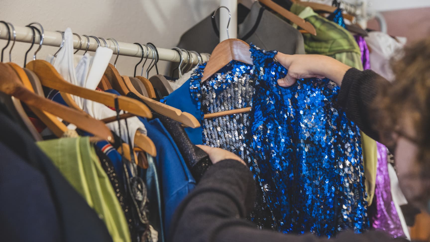 eine Person nimmt eine Jacke mit blauen Pailetten von einer Kleiderstange