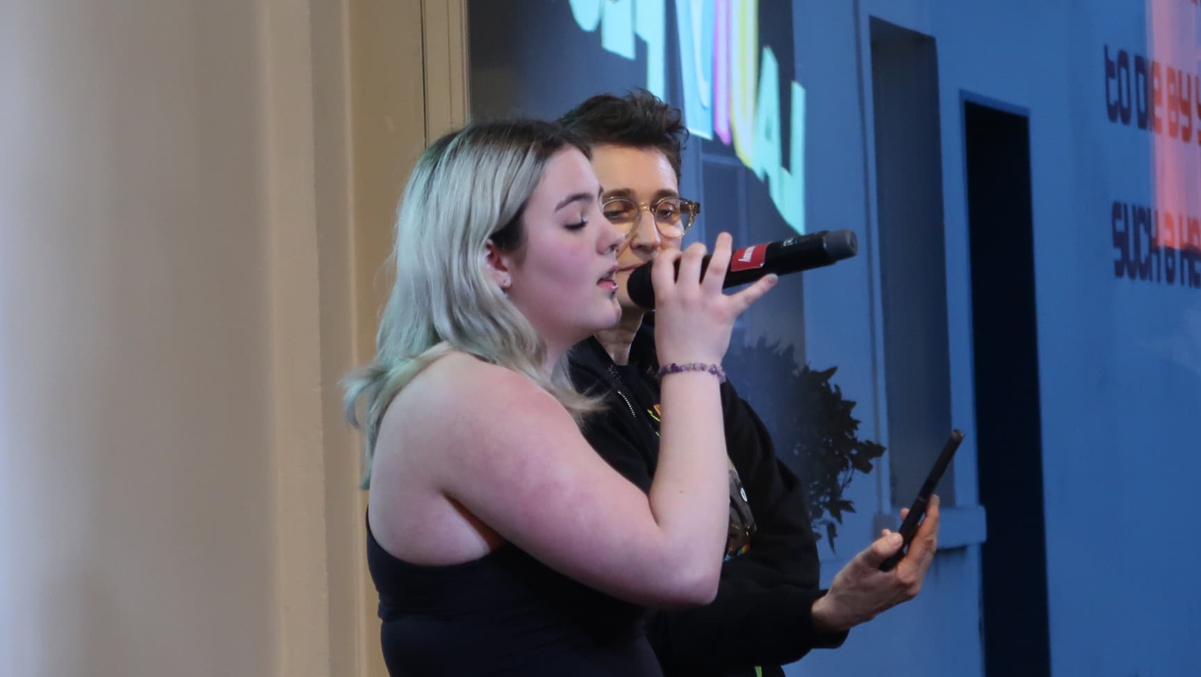 eine Person mit Mikrophon, eine Person hält ein Handy