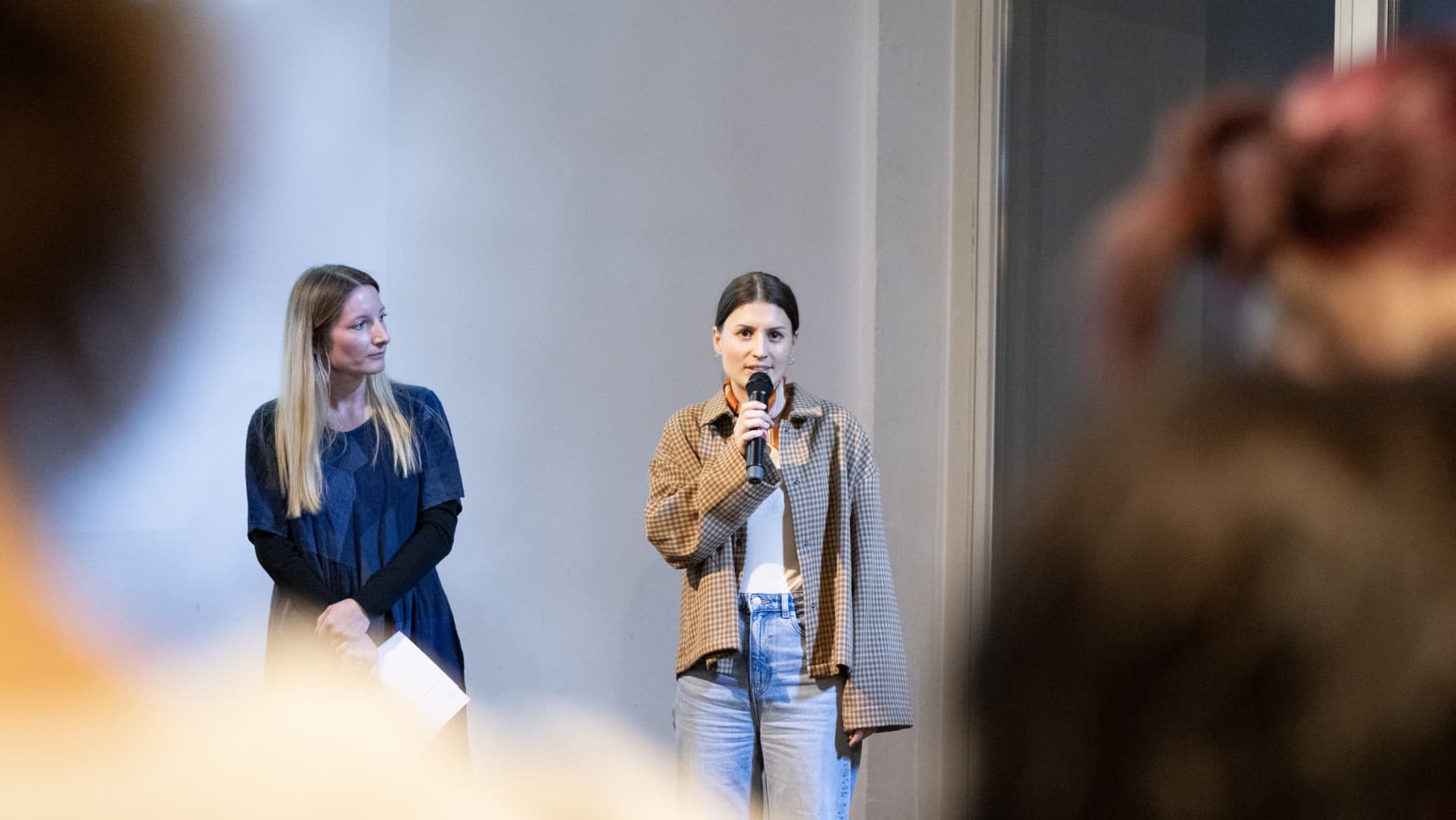 Zwei Frauen stehen nebeneinander. Eine spricht ins Mikrophon.