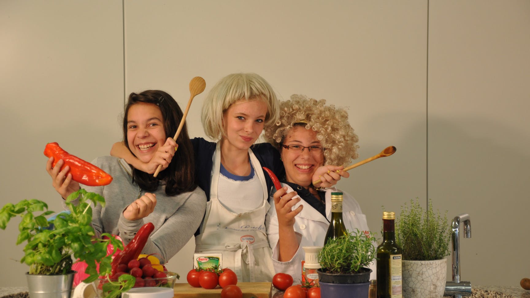 Drei verkleidete Jugendliche in einer Küche mit Kochlöffeln und Gemüse