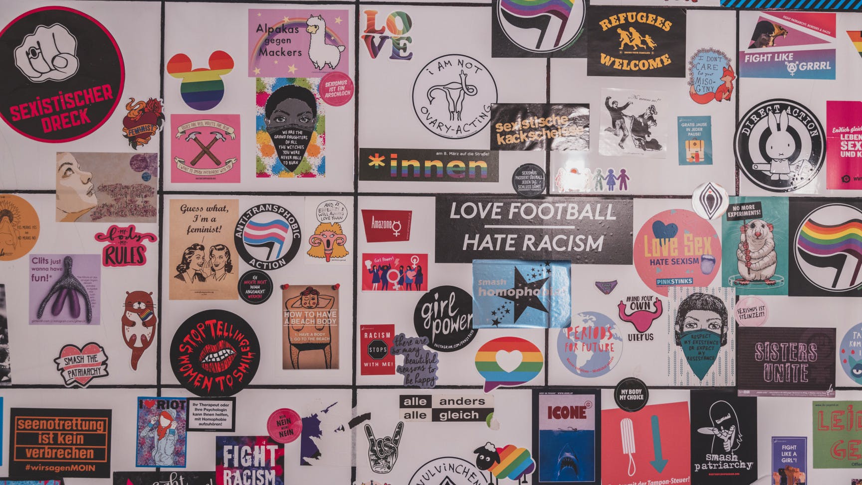 eine Wand mit vielen unterschiedlichen bunten Stickern – darauf sind queerfeministischen, intersektionalen Sprüche und Bilder zu sehen.