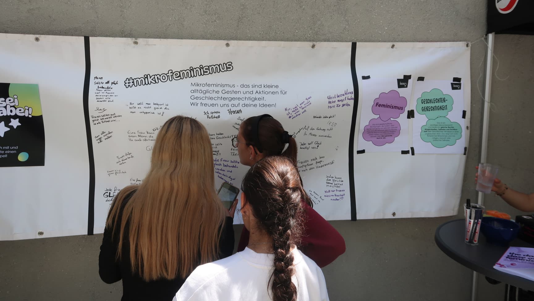 Drei Jugendliche stehen vor einem vollgeschriebenen Banner mit der Überschrift #mikrofeminismus