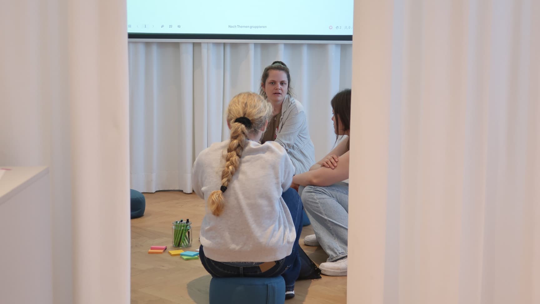 Drei Personen sitzen auf Sitzkissen und reden.