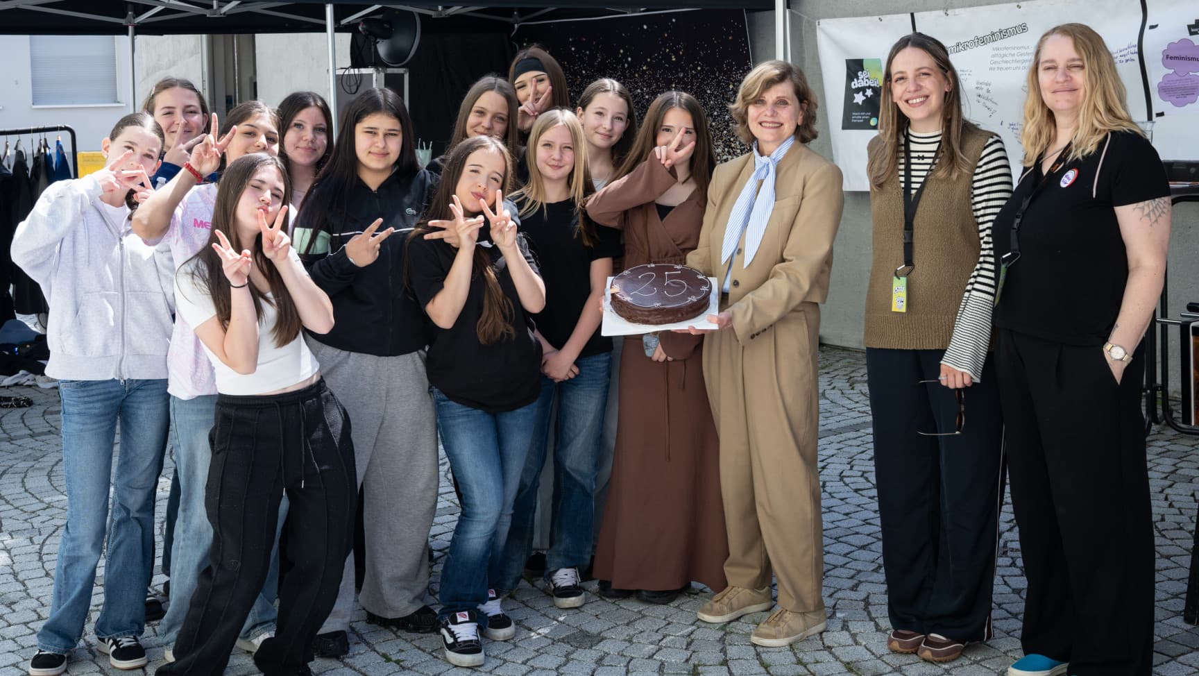 Eine Gruppe an Mädchen* und Frauen*. Eine Person hält einen Schokoladekuchen mit der Zahl 25.