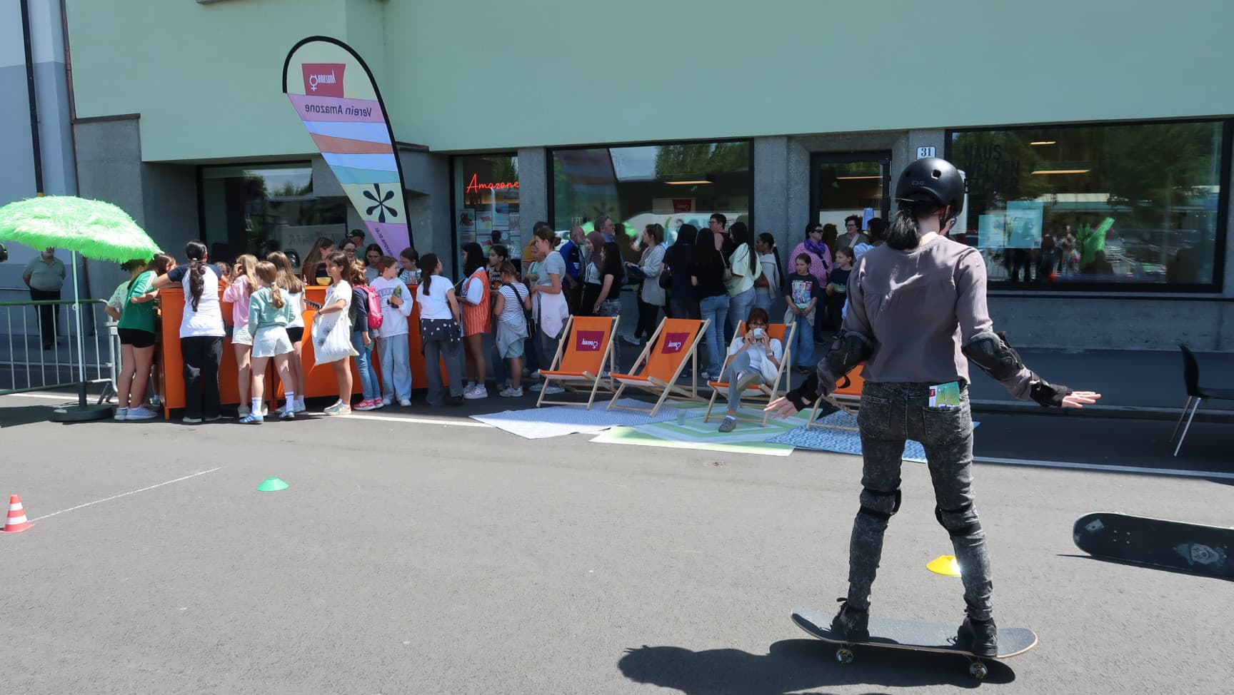 Person auf Skateboard. Hinten stehen viele Mädchen* an der amazoneBAR an.