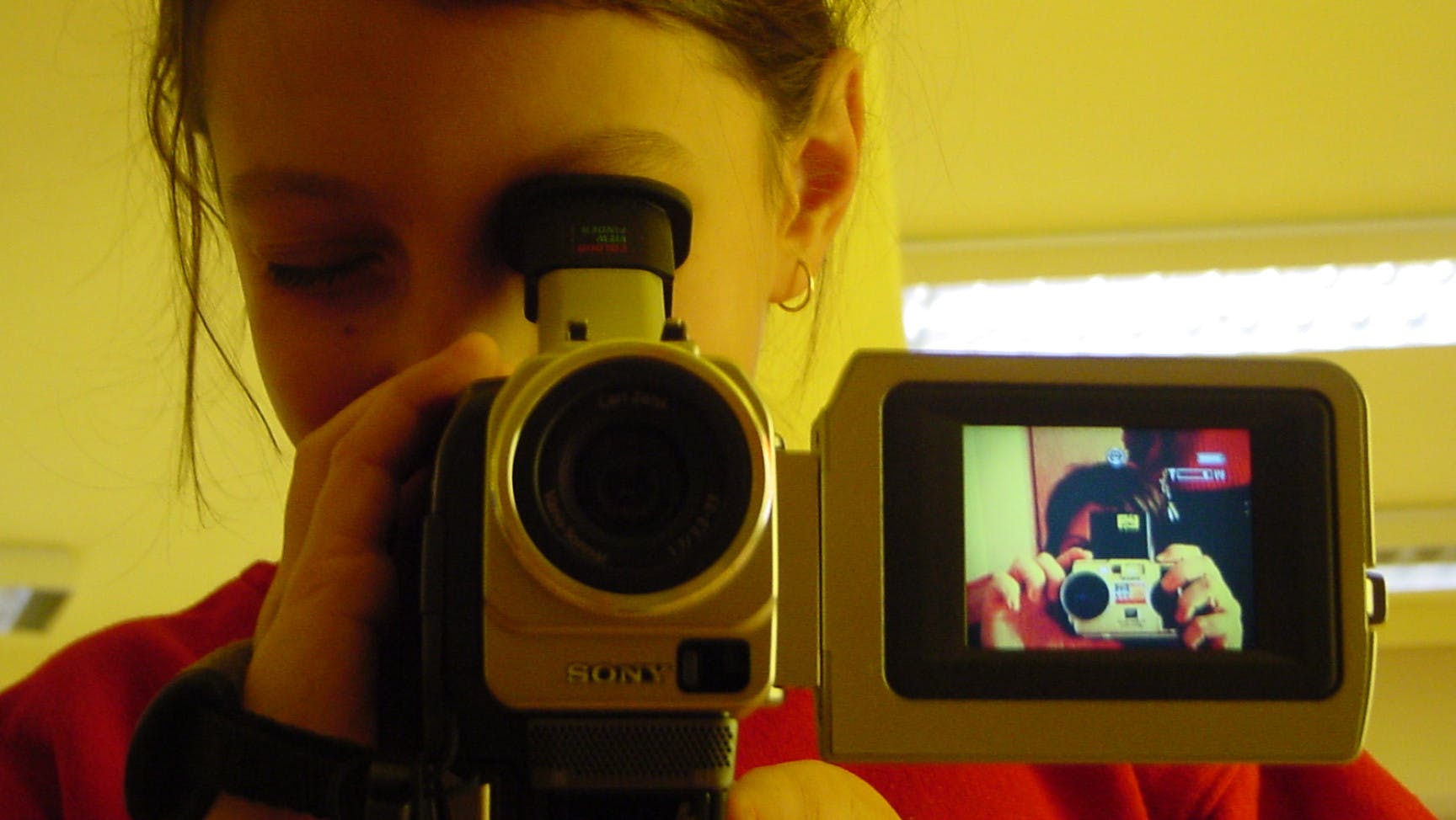 Eine jugendliche Person schaut durch den Sucher einer Videokamera.