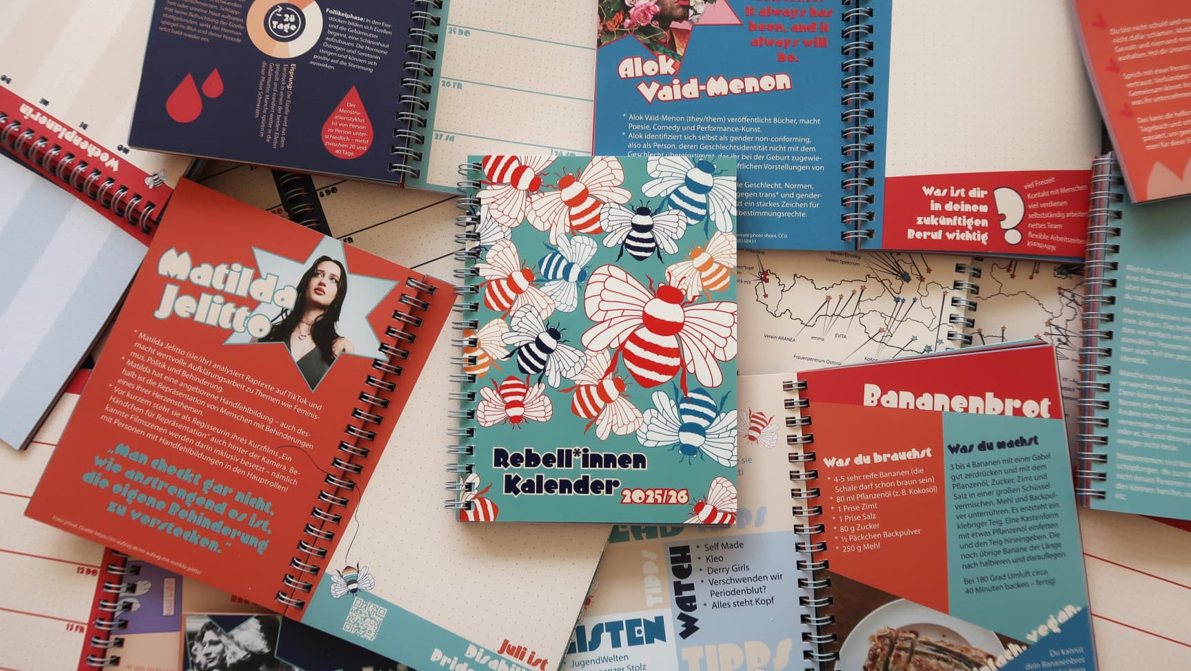 Der Rebell*innen Kalender liegt inmitten vieler aufgeschlagender Kalenderseiten.