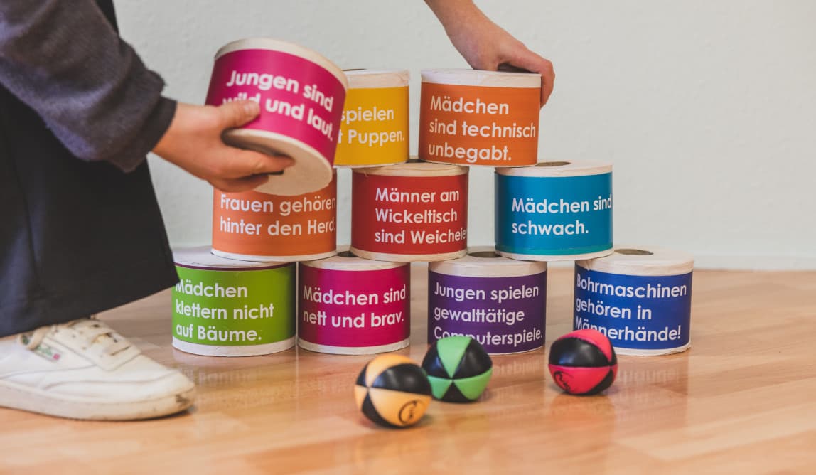 Klopapierrollen auf denen verschiedene Vorurteile stehen; eine Person stellt sie als Turm auf