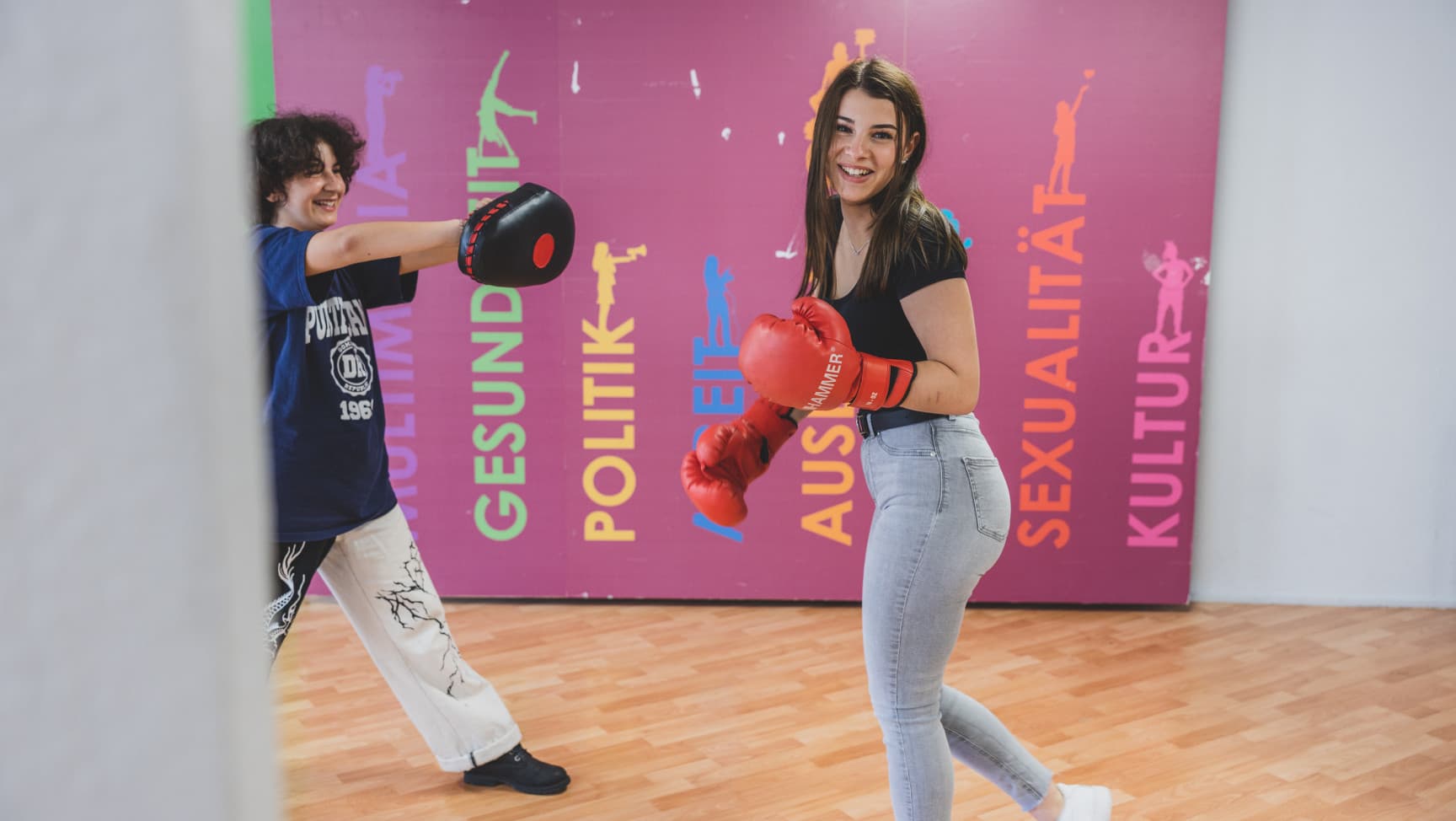 zwei Jugendliche mit Boxhandschuhen, eine der beiden lacht in die Kamera