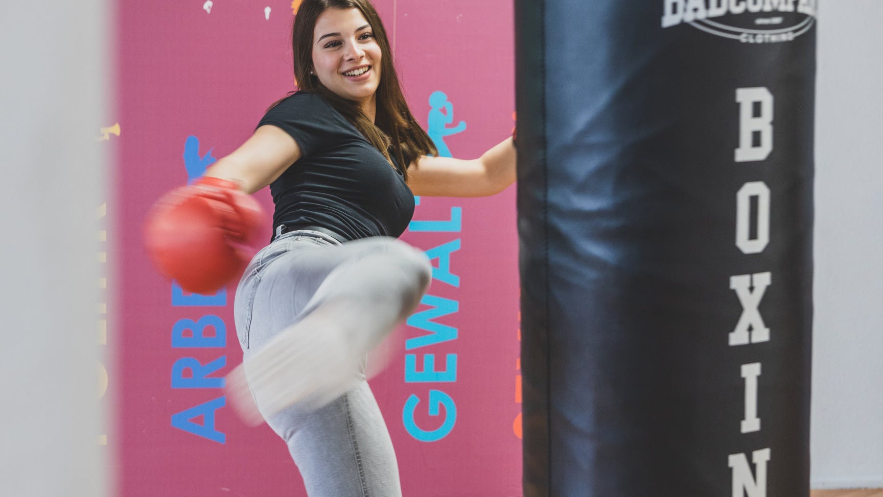 Junge Frau mit Boxhandschuhen kickt mit dem Fuß auf einen Boxsack