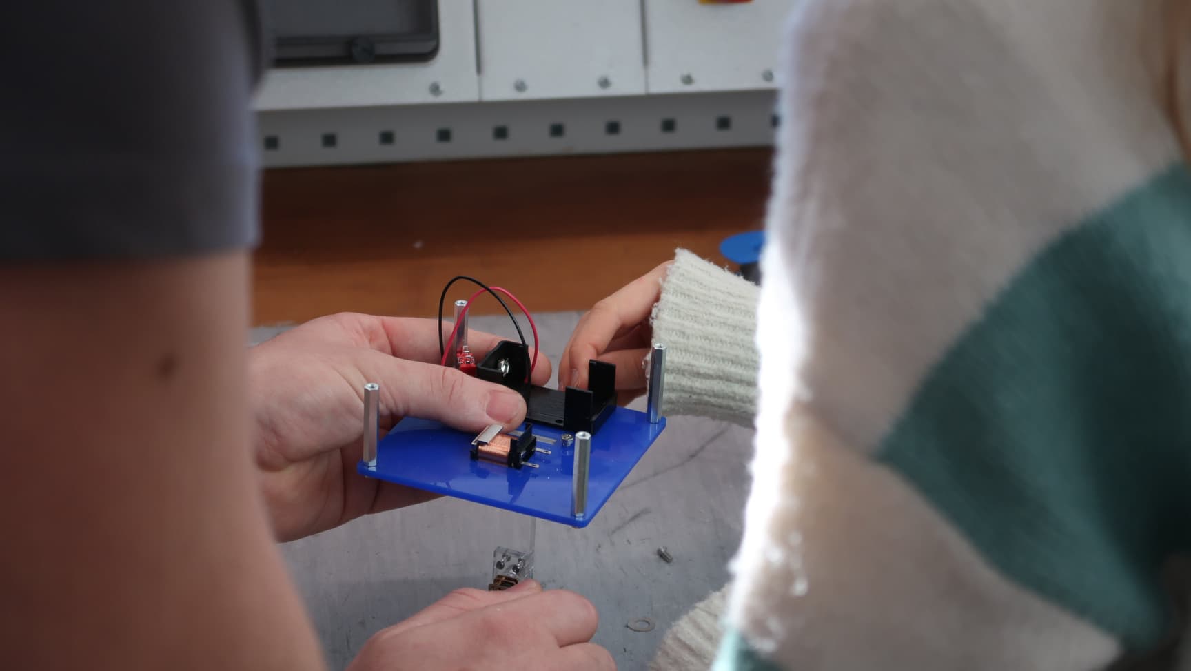 Zwei Personen halten eine kleine blaue Platte mit Kabeln in den Händen.